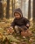 Maluch w ciemnobrązowym ponczu samochodowym z kapturem marki Albero Mio kuca w lesie przy prawdziwku z koszykiem grzybów.